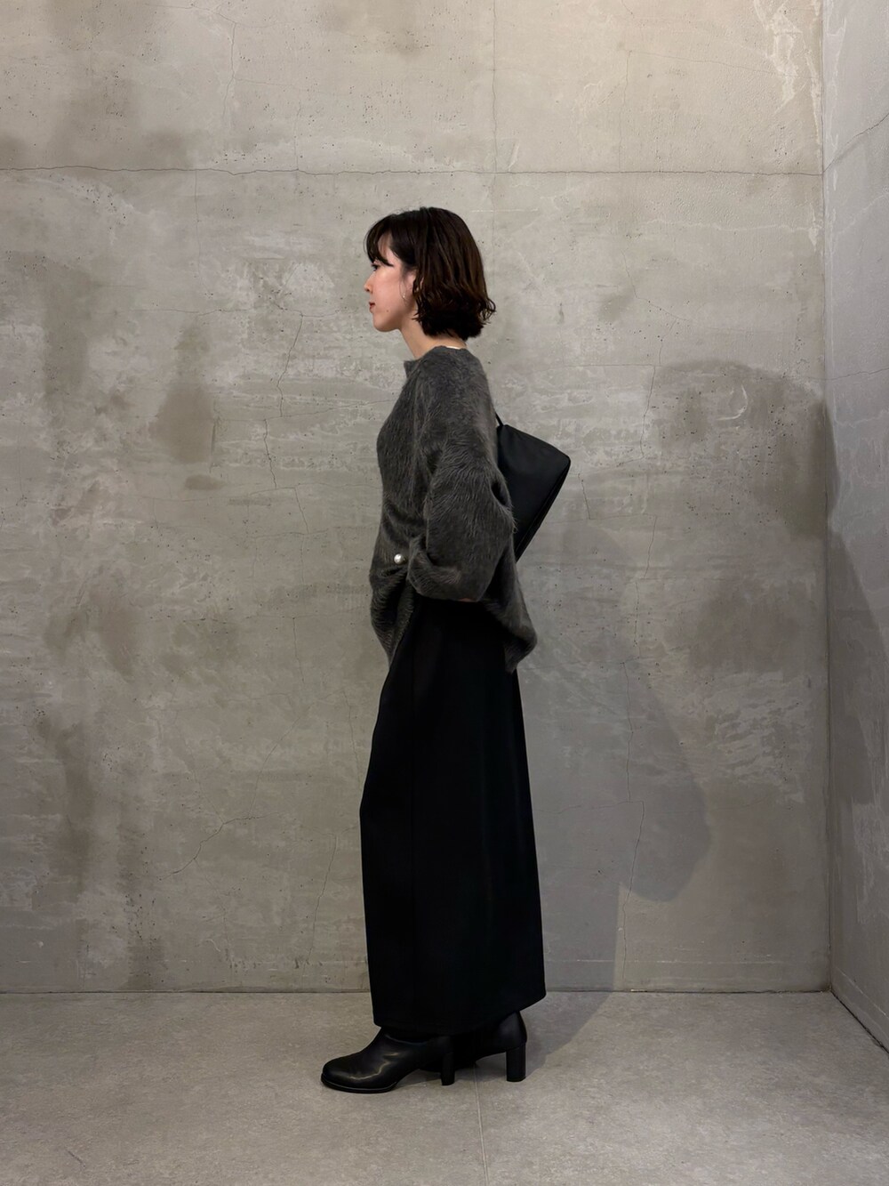 グレー系のニット/セーター、ブラック系のスカート、ホワイト系のTシャツ/カットソーを着用したレディースの秋コーディネートの2枚目の写真