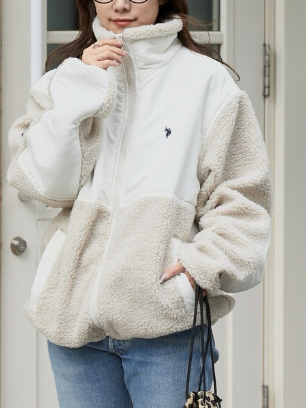 ホワイト系のブルゾン、ブルー系のデニムパンツ、ブラック系のメガネを着用したレディースの秋コーディネートの2枚目の写真