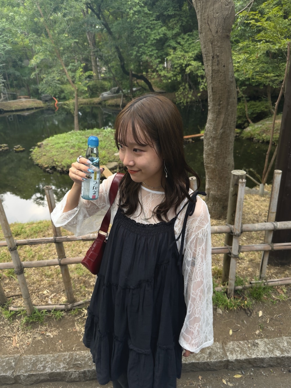 レッド系のショルダーバッグ、グレー系のスラックス、ブラック系のチュニックを着用したレディースの夏コーディネートの2枚目の写真