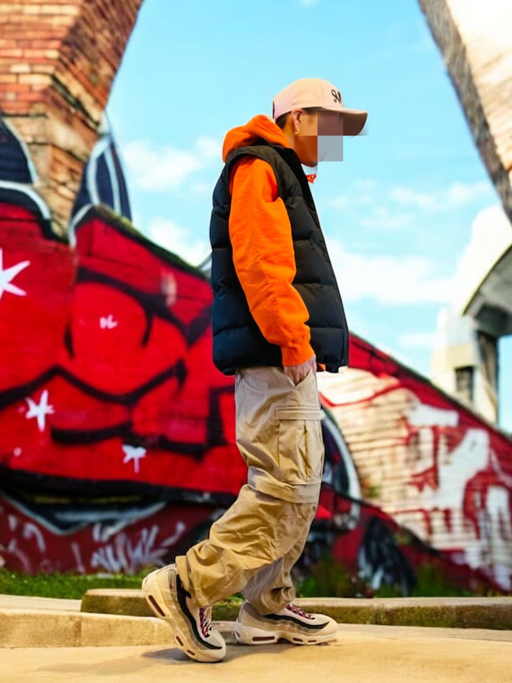 ブラック系のダウンベスト、オレンジ系のパーカー、ベージュ系のカーゴパンツを着用したメンズの秋コーディネートの2枚目の写真