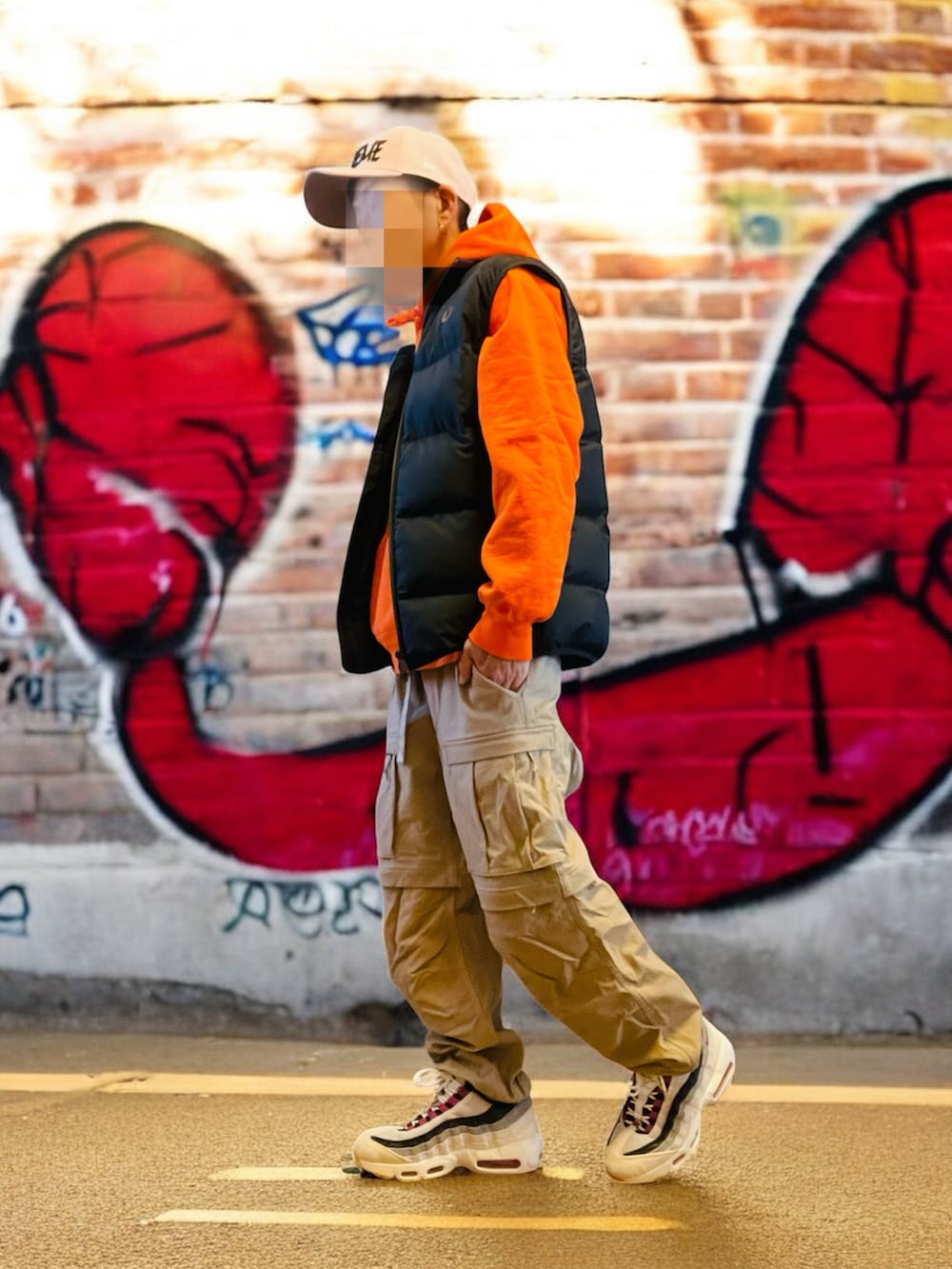 ブラック系のダウンベスト、オレンジ系のパーカー、ベージュ系のカーゴパンツを着用したメンズの秋コーディネートの3枚目の写真