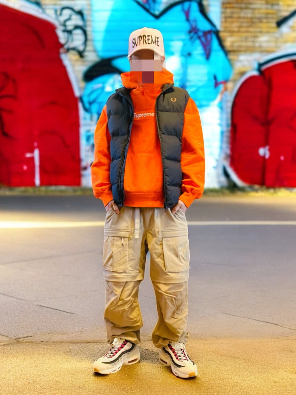 ブラック系のダウンベスト、オレンジ系のパーカー、ベージュ系のカーゴパンツを着用したメンズの秋コーディネートの4枚目の写真