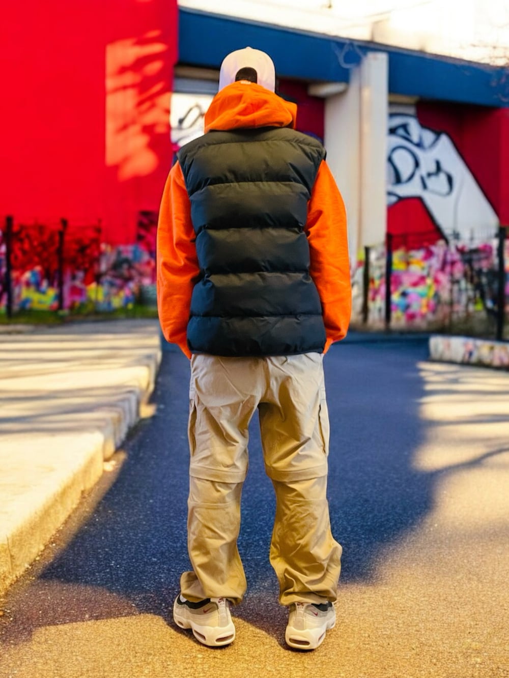 ブラック系のダウンベスト、オレンジ系のパーカー、ベージュ系のカーゴパンツを着用したメンズの秋コーディネートの5枚目の写真