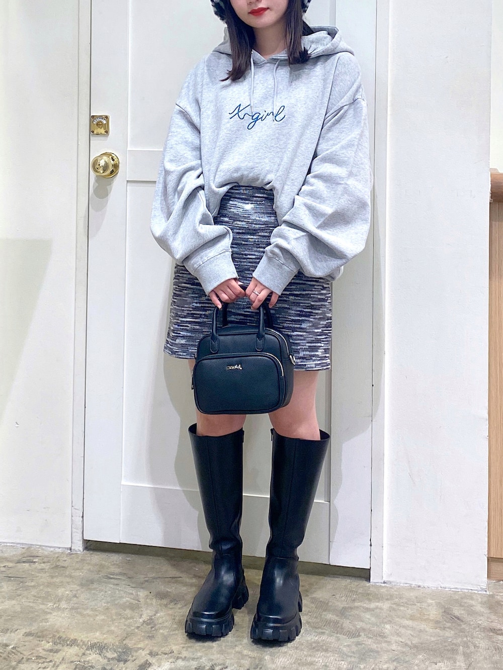 グレー系のパーカー、ブラック系のスカート、ブラック系のブーツを着用したレディースの秋コーディネートの2枚目の写真