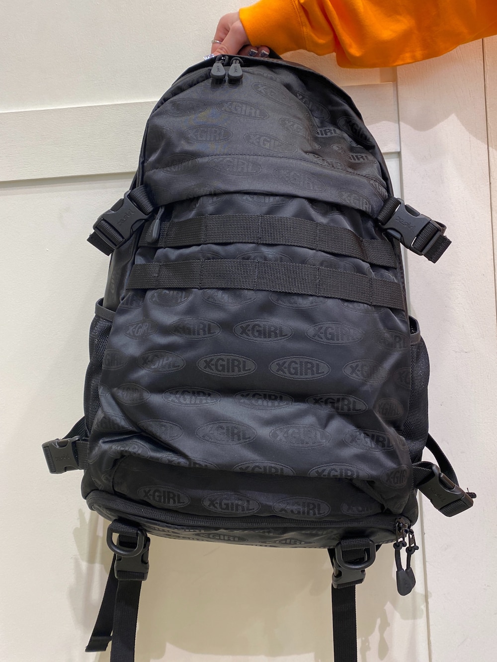 オレンジ系のTシャツ/カットソー、ブラック系のバックパック/リュック、ブラック系のその他パンツを着用したレディースの春コーディネートの2枚目の写真