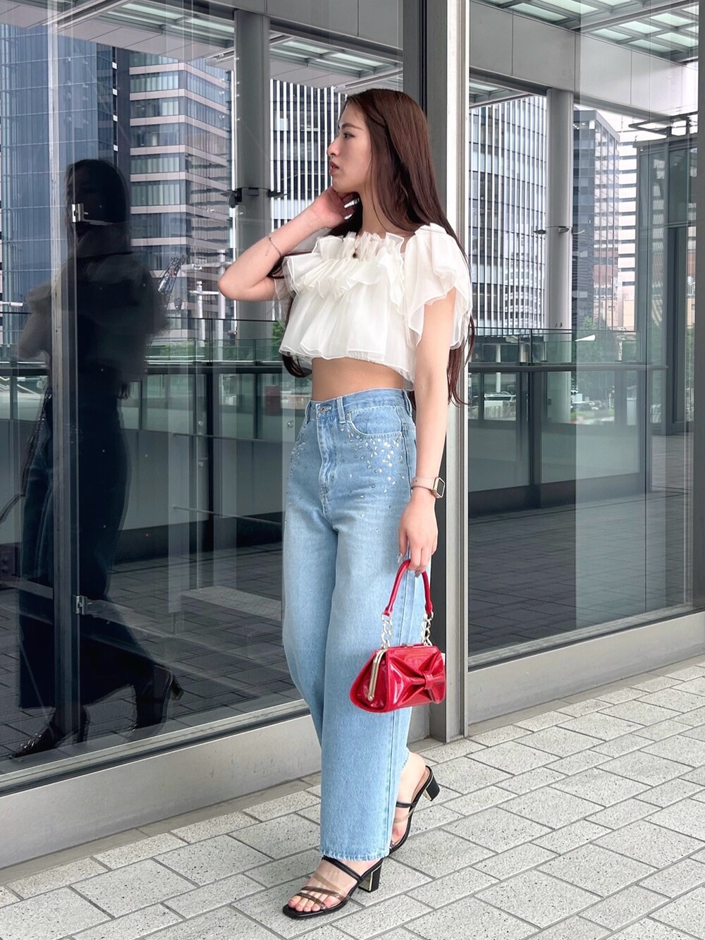 レッド系のハンドバッグ、ホワイト系のシャツ/ブラウス、ブルー系のデニムパンツを着用したレディースの春コーディネートの2枚目の写真