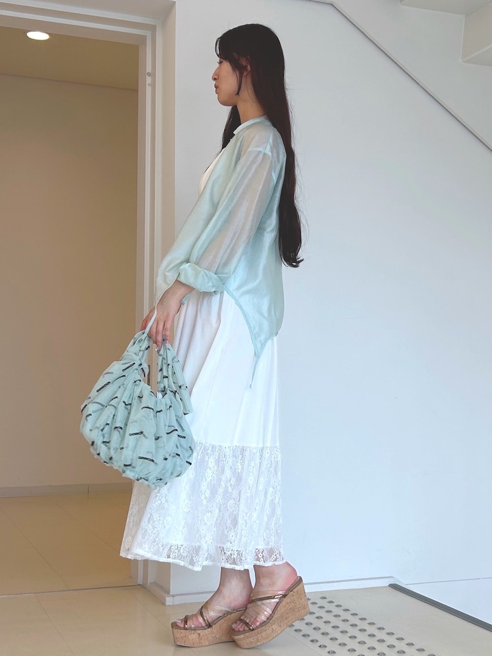 グリーン系のハンドバッグ、ホワイト系のワンピース、ブラウン系のサンダルを着用したレディースの夏コーディネートの2枚目の写真