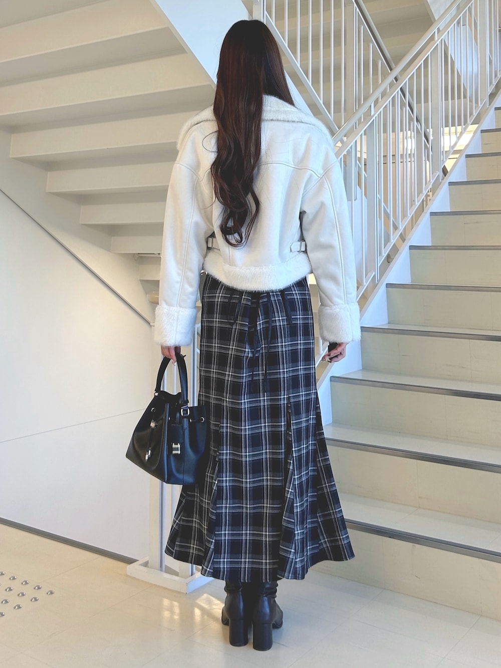 ブラック系のスカート、ホワイト系のムートンコート、ブラウン系のニット/セーターを着用したレディースの秋コーディネートの4枚目の写真