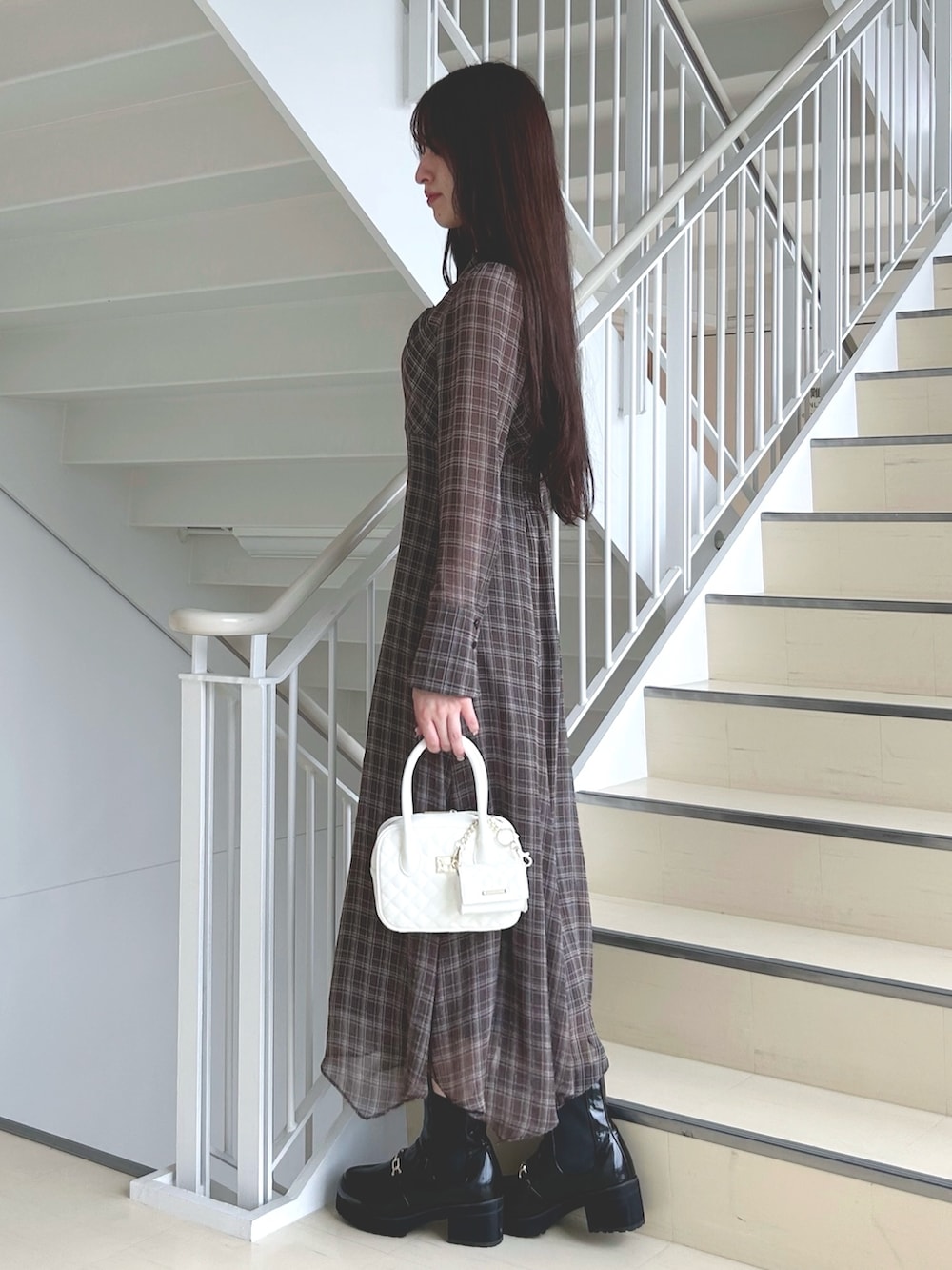 ブラウン系のワンピース、ホワイト系のハンドバッグ、ブラック系のブーツを着用したレディースの秋コーディネートの2枚目の写真