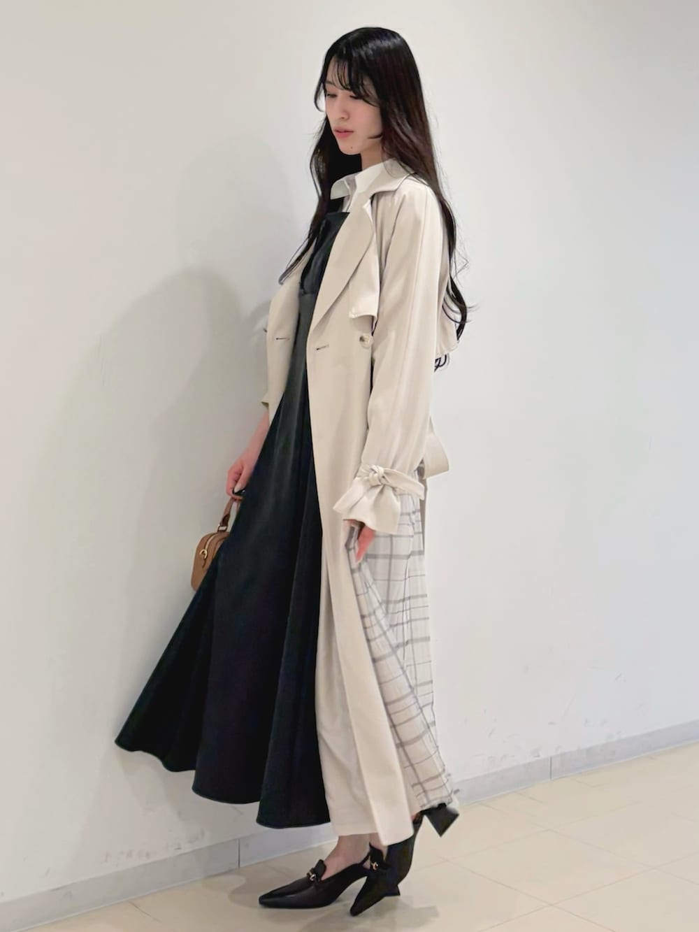 ブラック系のワンピース、ベージュ系のトレンチコート、ブラウン系のハンドバッグを着用したレディースの冬コーディネートの3枚目の写真