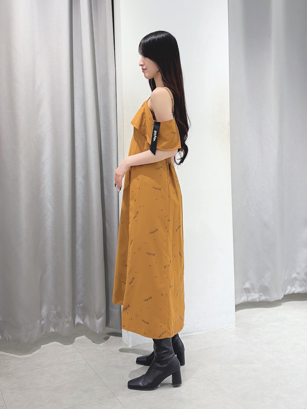 イエロー系のワンピース、ブラウン系のショルダーバッグ、ブラウン系のブーツを着用したレディースの夏コーディネートの2枚目の写真
