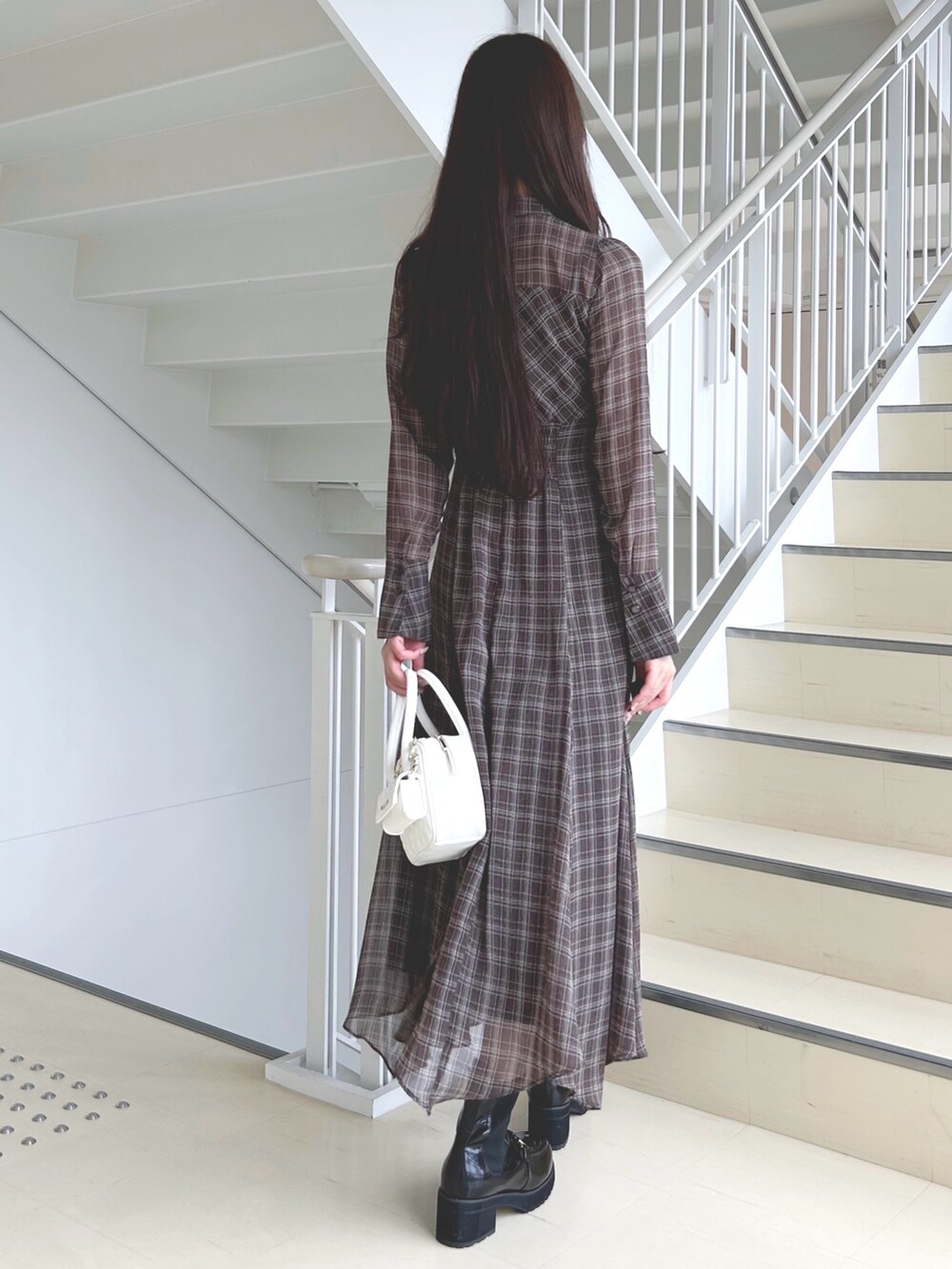 ブラウン系のワンピース、ホワイト系のハンドバッグ、ブラック系のブーツを着用したレディースの秋コーディネートの4枚目の写真