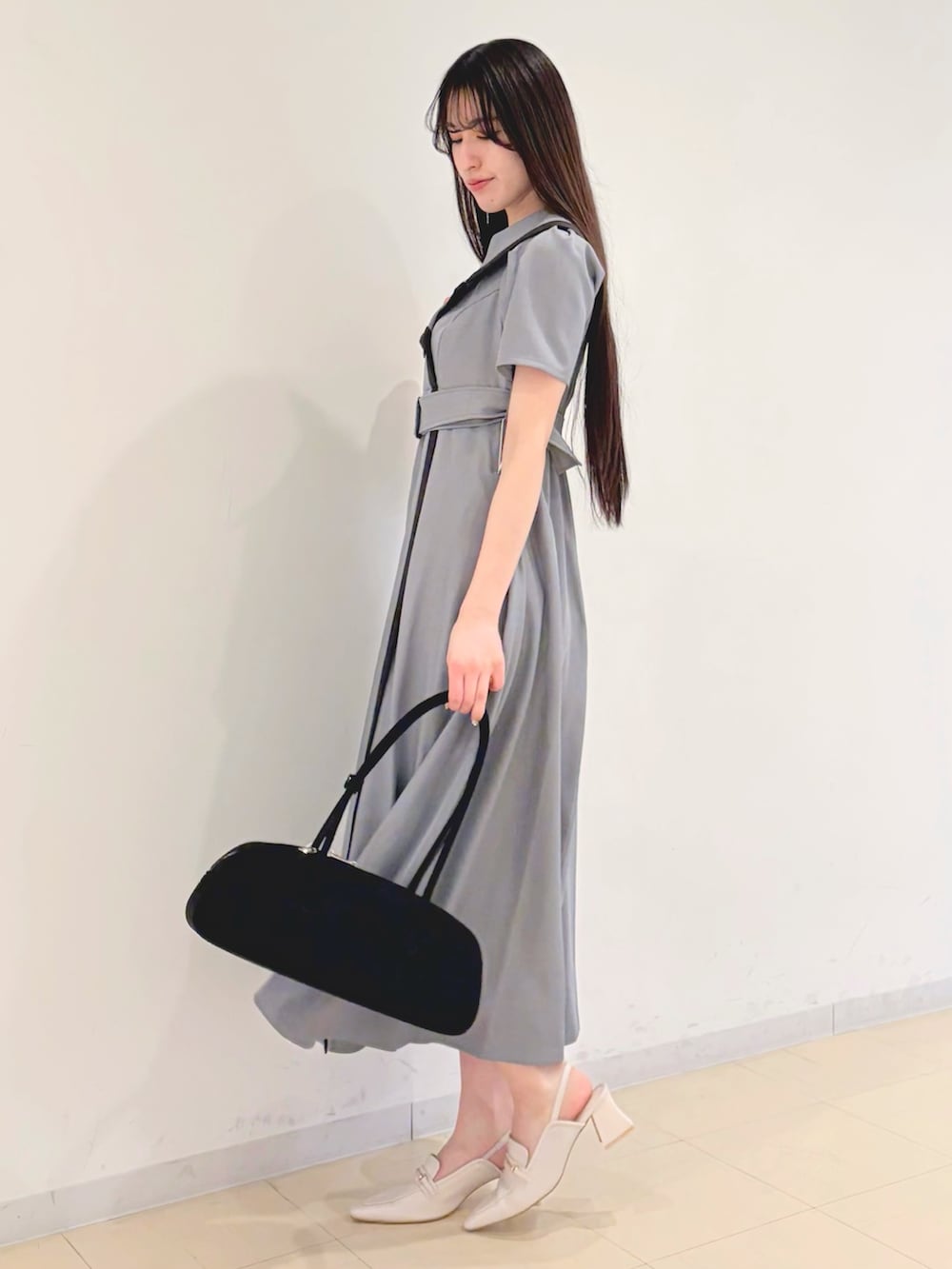 グレー系のワンピース、ブラック系のハンドバッグ、ホワイト系のパンプスを着用したレディースの春コーディネートの2枚目の写真