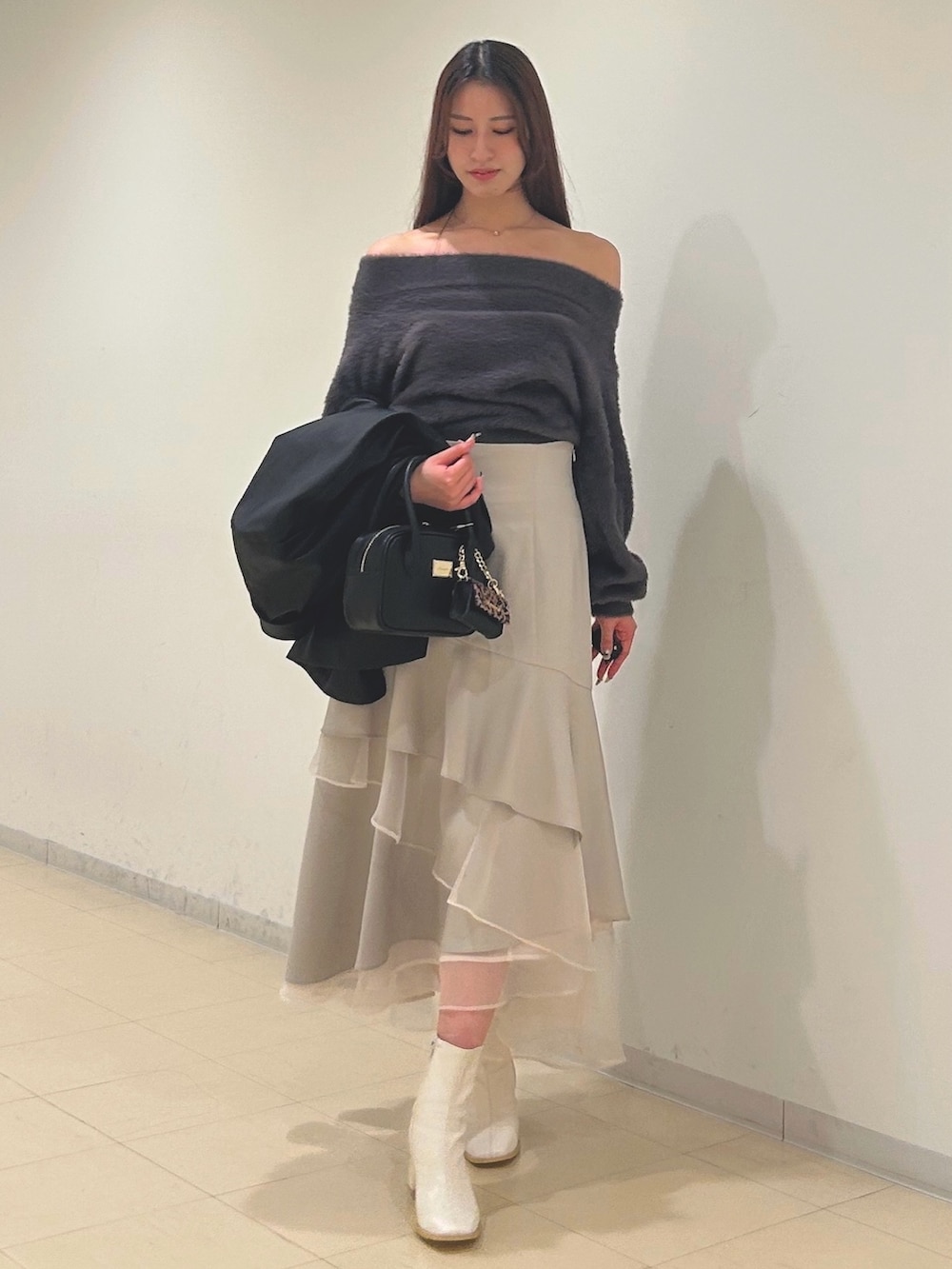 ベージュ系のスカート、グレー系のニット/セーター、ブラック系のハンドバッグを着用したレディースの秋コーディネートの3枚目の写真