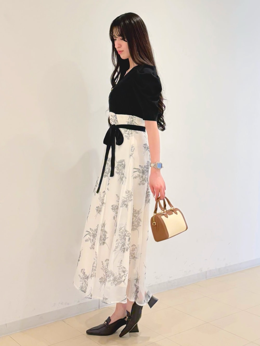 ブラック系のワンピース、ブラウン系のハンドバッグ、ブラウン系のパンプスを着用したレディースの春コーディネートの2枚目の写真