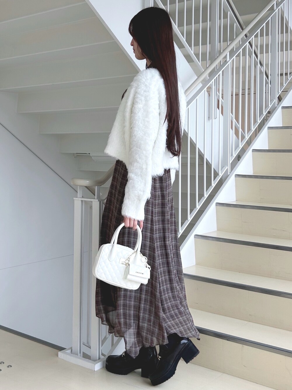 ブラウン系のワンピース、ホワイト系のハンドバッグ、ブラック系のブーツを着用したレディースの秋コーディネートの2枚目の写真