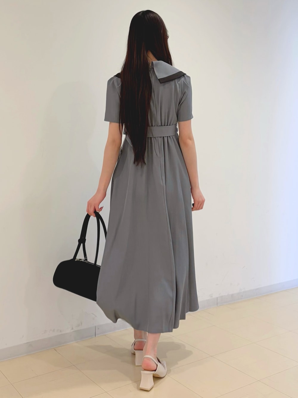 グレー系のワンピース、ブラック系のハンドバッグ、ホワイト系のパンプスを着用したレディースの春コーディネートの3枚目の写真