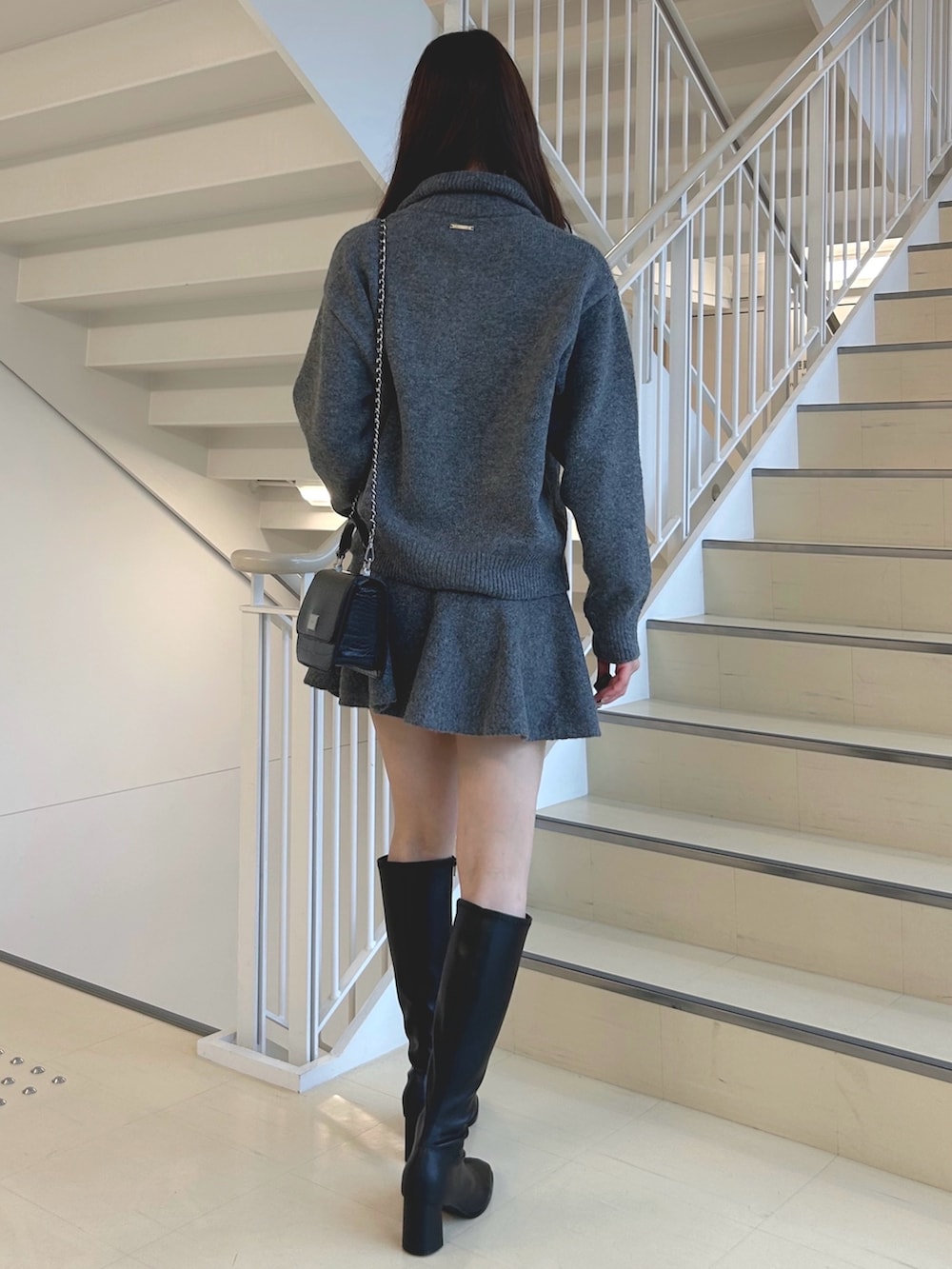 グレー系のワンピース、ブラック系のブーツ、ブラック系のハンドバッグを着用したレディースの秋コーディネートの4枚目の写真