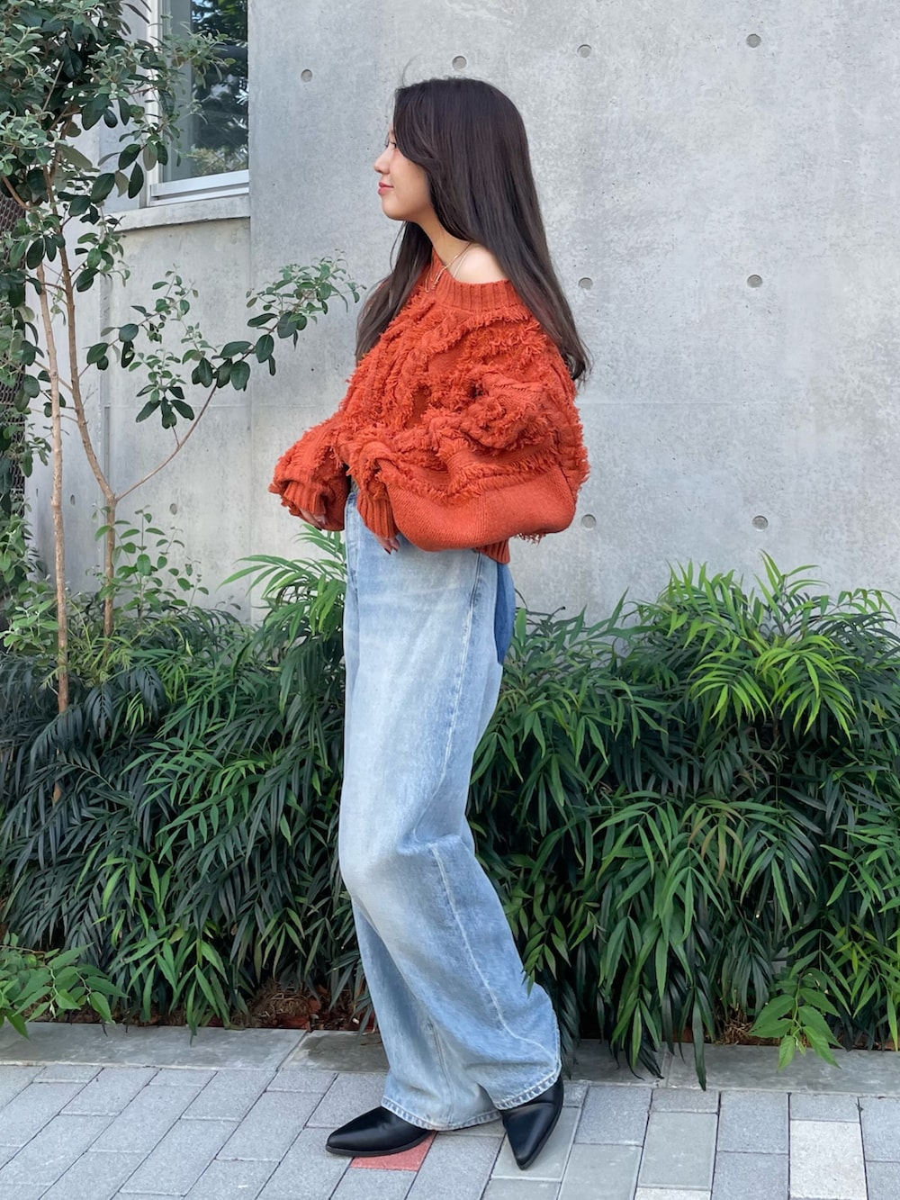 ブルー系のデニムパンツ、ブラック系のブーツ、オレンジ系のニット/セーターを着用したレディースの秋コーディネートの2枚目の写真