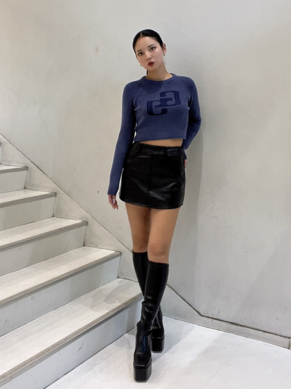 ブルー系のニット/セーター、ブラック系のスカート、ブラック系のブーツを着用したレディースの秋コーディネートの2枚目の写真