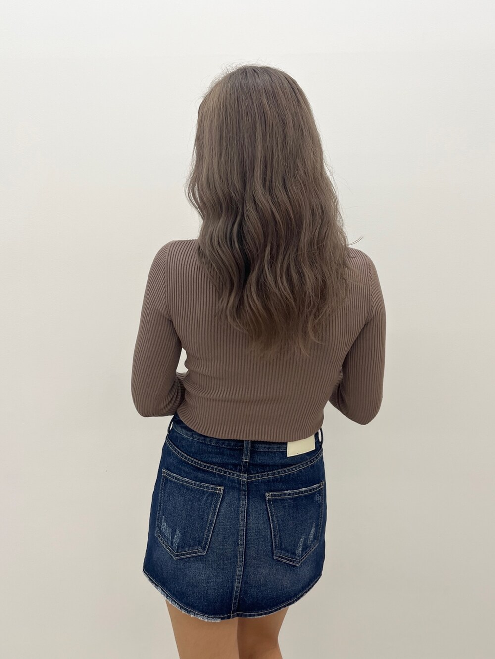 ベージュ系のニット/セーター、ブルー系のデニムスカート、ブラウン系のブーツを着用したレディースの秋コーディネートの4枚目の写真