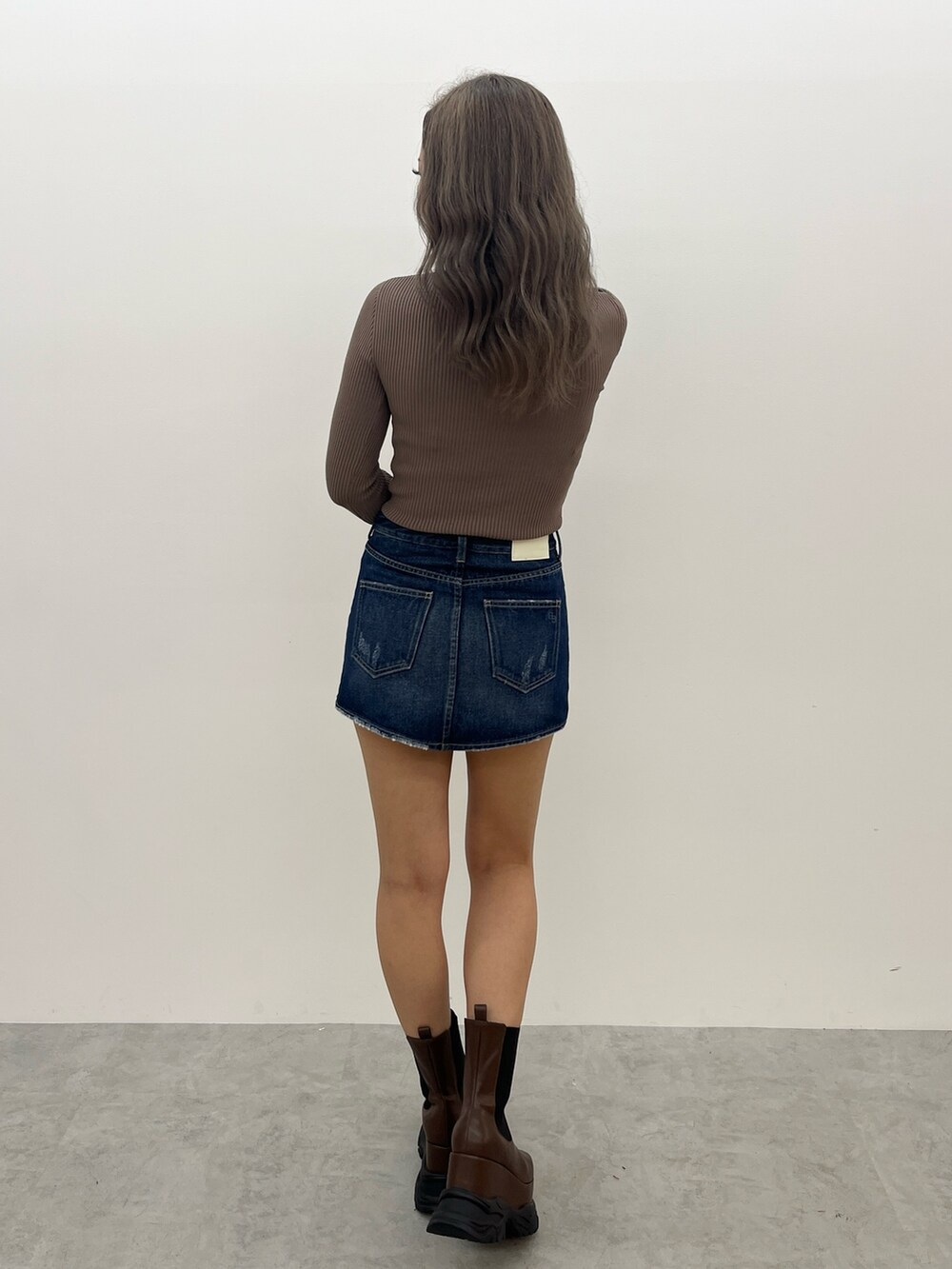 ベージュ系のニット/セーター、ブルー系のデニムスカート、ブラウン系のブーツを着用したレディースの秋コーディネートの2枚目の写真