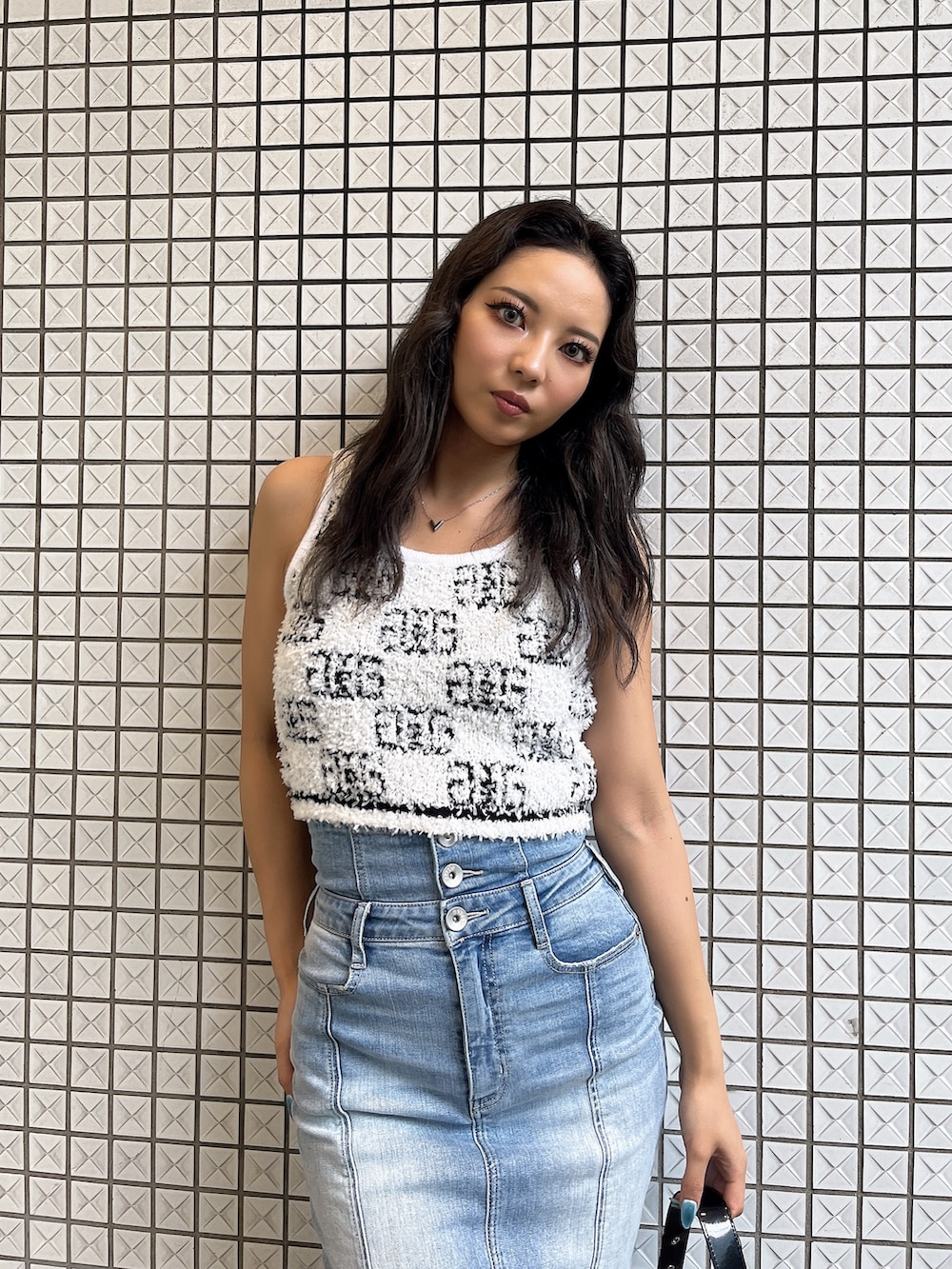 ホワイト系のニット/セーター、ブルー系のデニムスカート、ブラック系のハンドバッグを着用したレディースの夏コーディネートの2枚目の写真