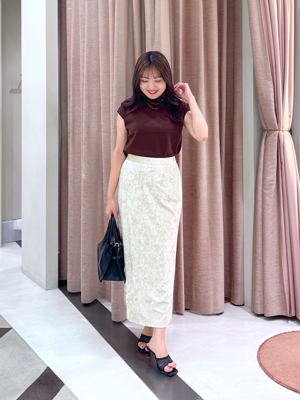 ブラウン系のニット/セーター、ベージュ系のスカート、ブラック系のトートバッグを着用したレディースの夏コーディネートの2枚目の写真