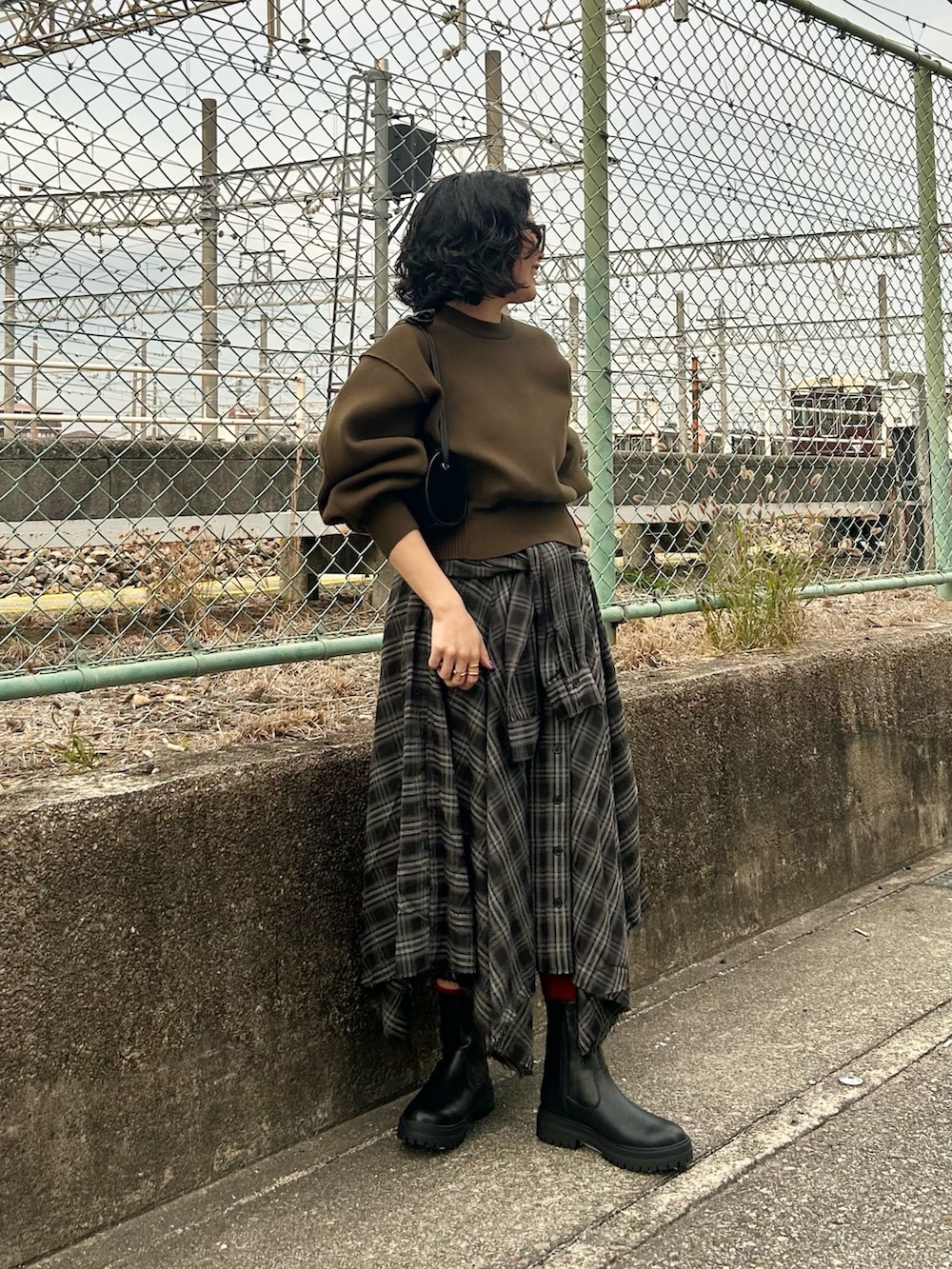 グリーン系のニット/セーター、ブラック系のスカート、ブラック系のブーツを着用したレディースの冬コーディネートの2枚目の写真