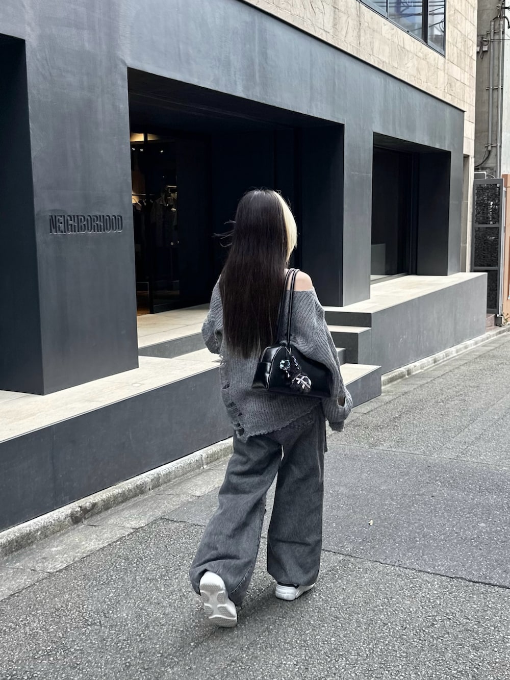 ブラック系のデニムパンツ、ホワイト系のスニーカー、グレー系のニット/セーターを着用したレディースの秋コーディネートの2枚目の写真