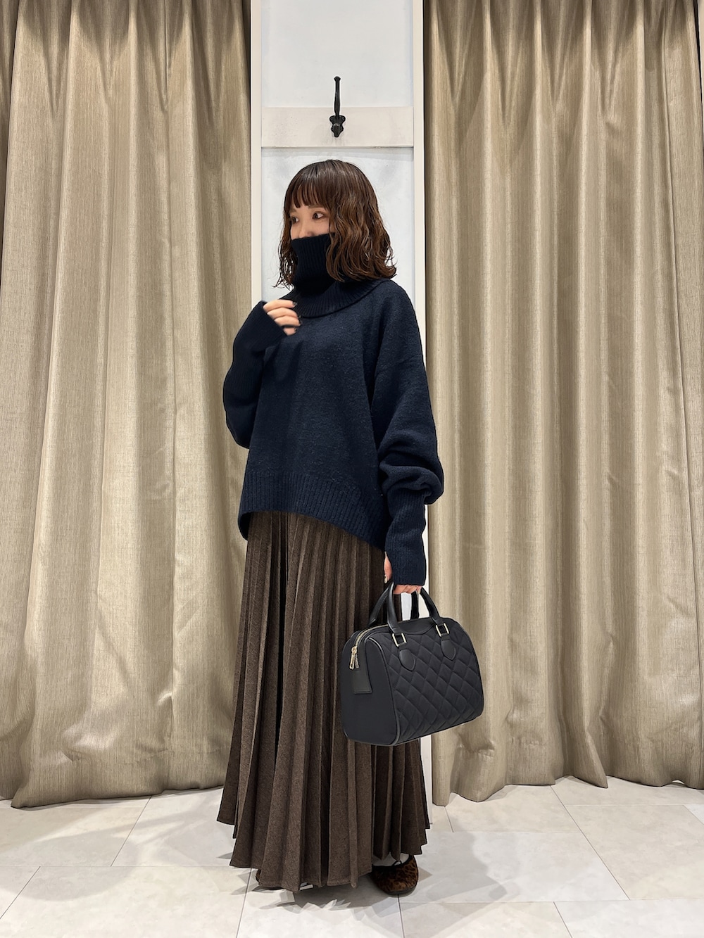 ブルー系のニット/セーター、ブラウン系のスカート、ベージュ系のハンドバッグを着用したレディースの秋コーディネートの3枚目の写真