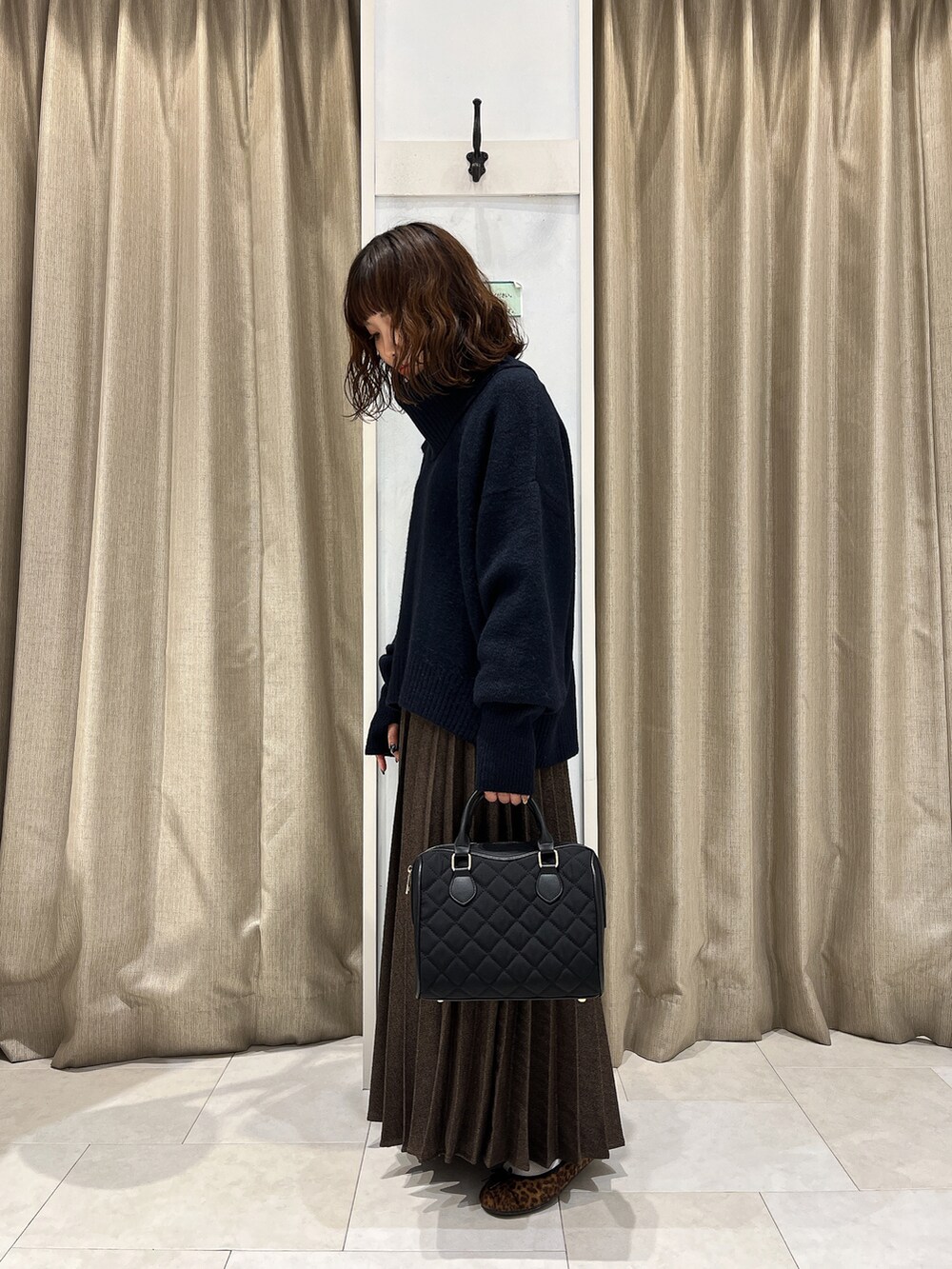 ブルー系のニット/セーター、ブラウン系のスカート、ベージュ系のハンドバッグを着用したレディースの秋コーディネートの2枚目の写真