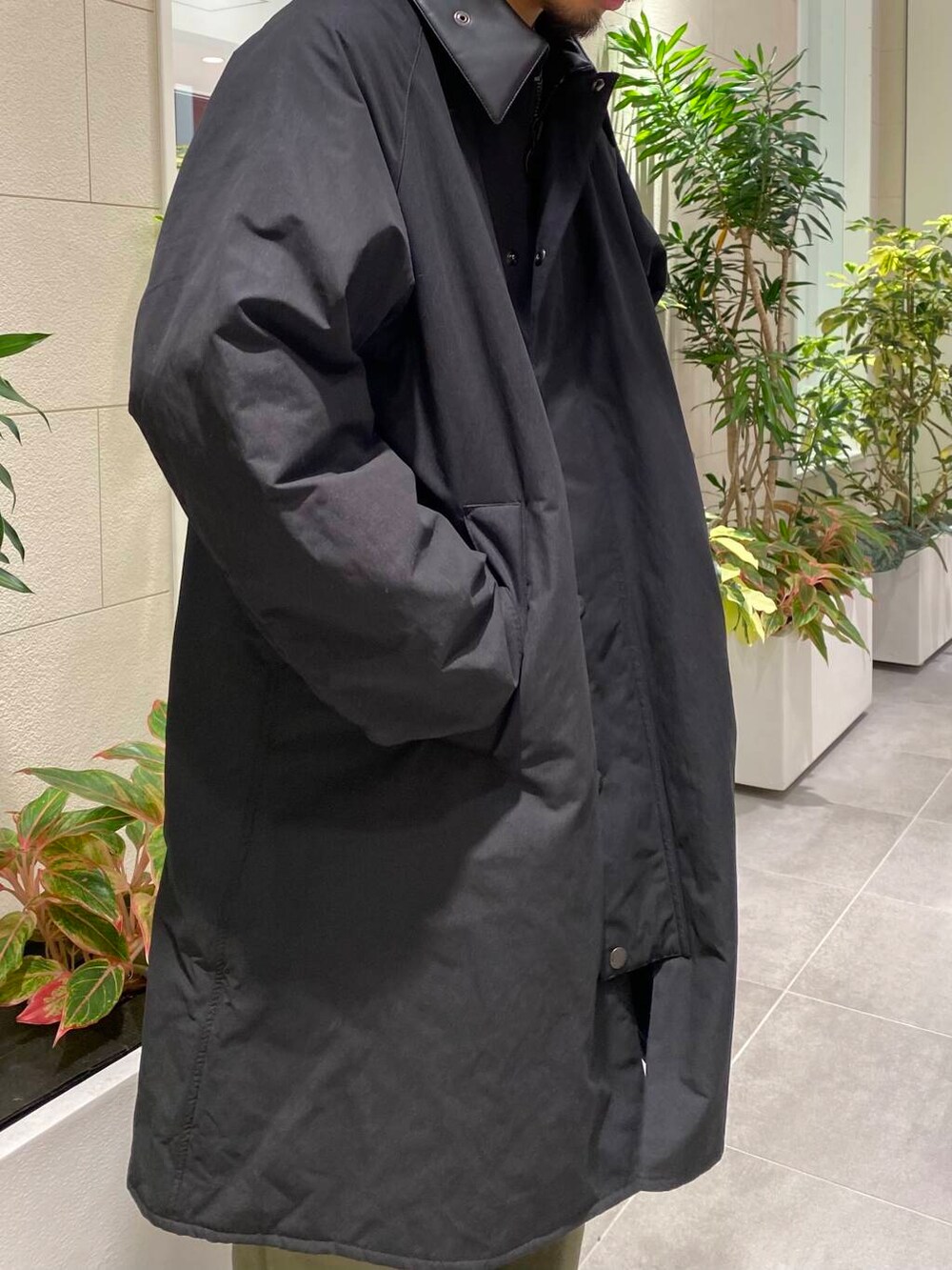 ブラック系のスニーカー、ブラック系のステンカラーコート、グリーン系のチノパンツを着用したメンズの冬コーディネートの2枚目の写真