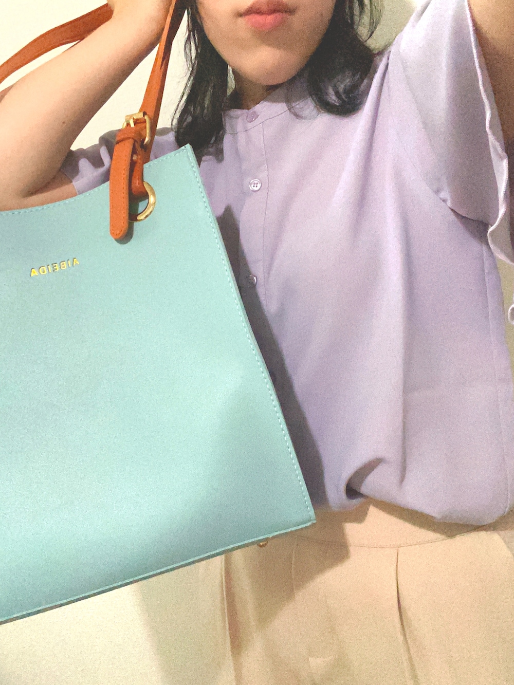 ベージュ系のスラックス、ブルー系のハンドバッグ、パープル系のシャツ/ブラウスを着用したレディースの夏コーディネートの2枚目の写真