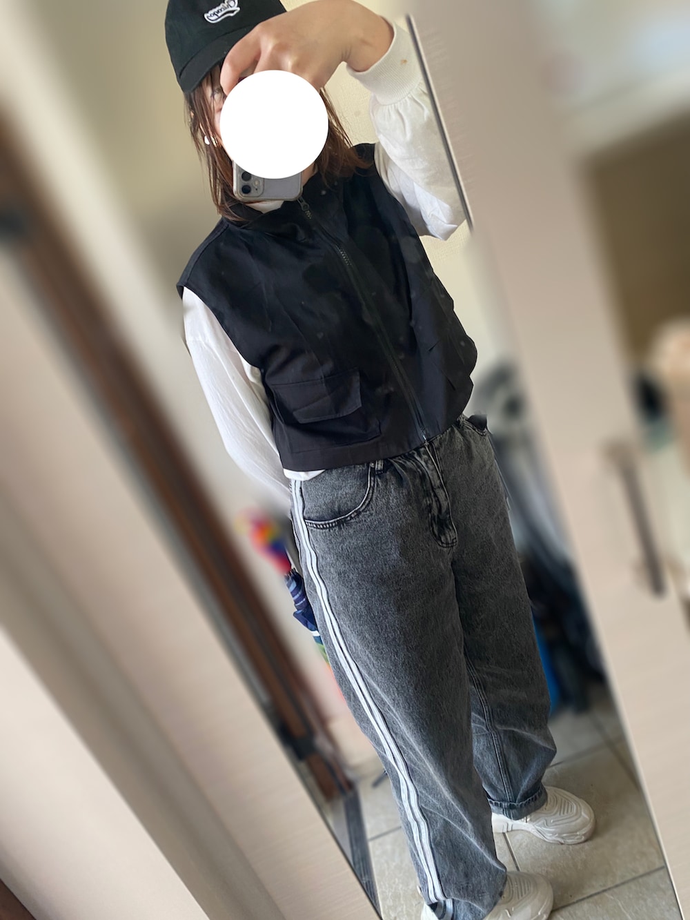 グレー系のデニムパンツ、ホワイト系のスニーカー、ブラック系のベストを着用したレディースの春コーディネートの2枚目の写真