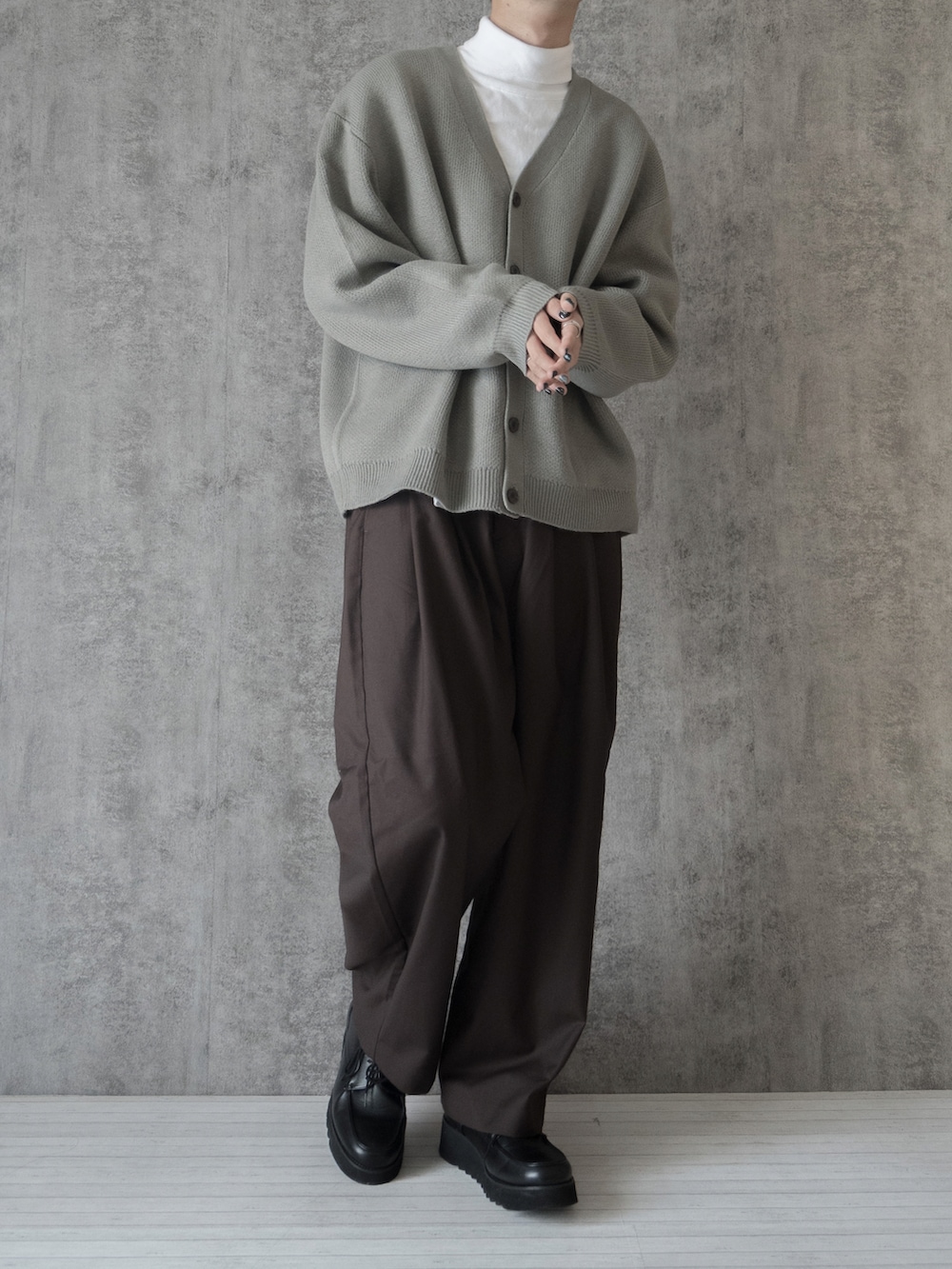グレー系のカーディガン/ボレロ、ホワイト系のTシャツ/カットソー、ブラウン系のスラックスを着用したメンズの冬コーディネートの2枚目の写真