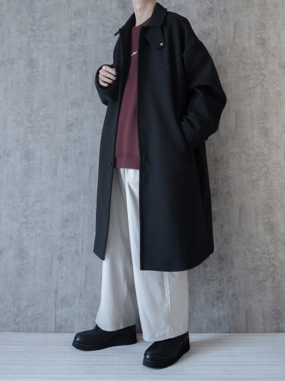 ブラック系のステンカラーコート、ホワイト系のスラックスを着用したメンズの冬コーディネートの2枚目の写真