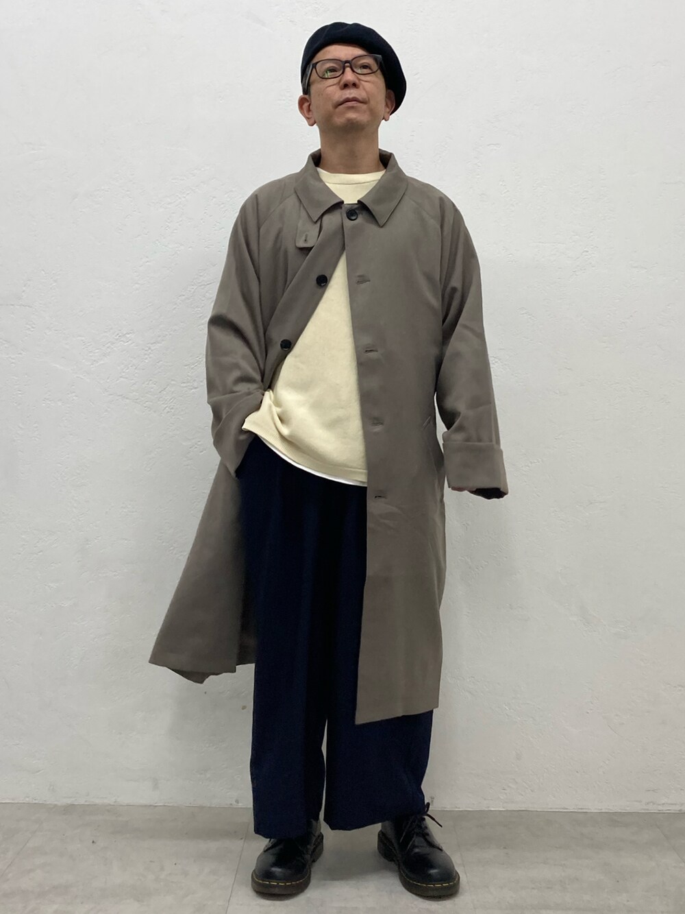 ベージュ系のステンカラーコート、ブルー系のスラックス、ブラック系のドレスシューズを着用したメンズの秋コーディネートの2枚目の写真