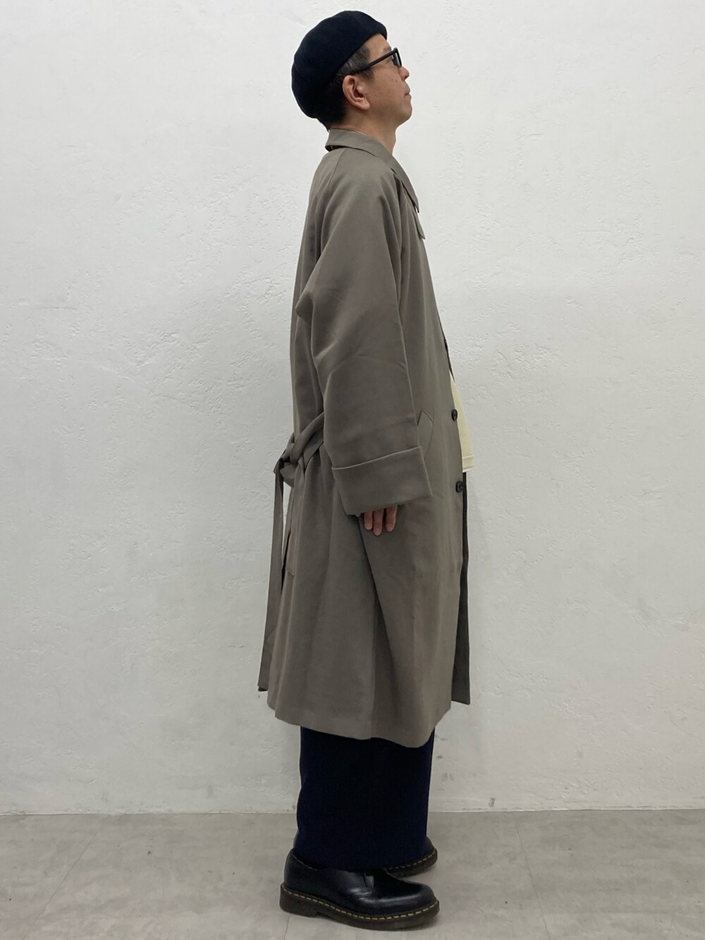 ベージュ系のステンカラーコート、ブルー系のスラックス、ブラック系のドレスシューズを着用したメンズの秋コーディネートの3枚目の写真