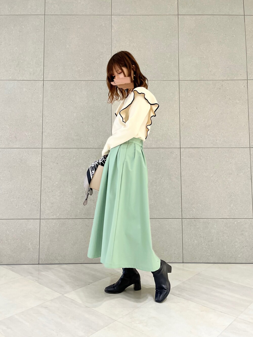 ホワイト系のニット/セーター、ベージュ系のハンドバッグ、グリーン系のスカートを着用したレディースの冬コーディネートの2枚目の写真