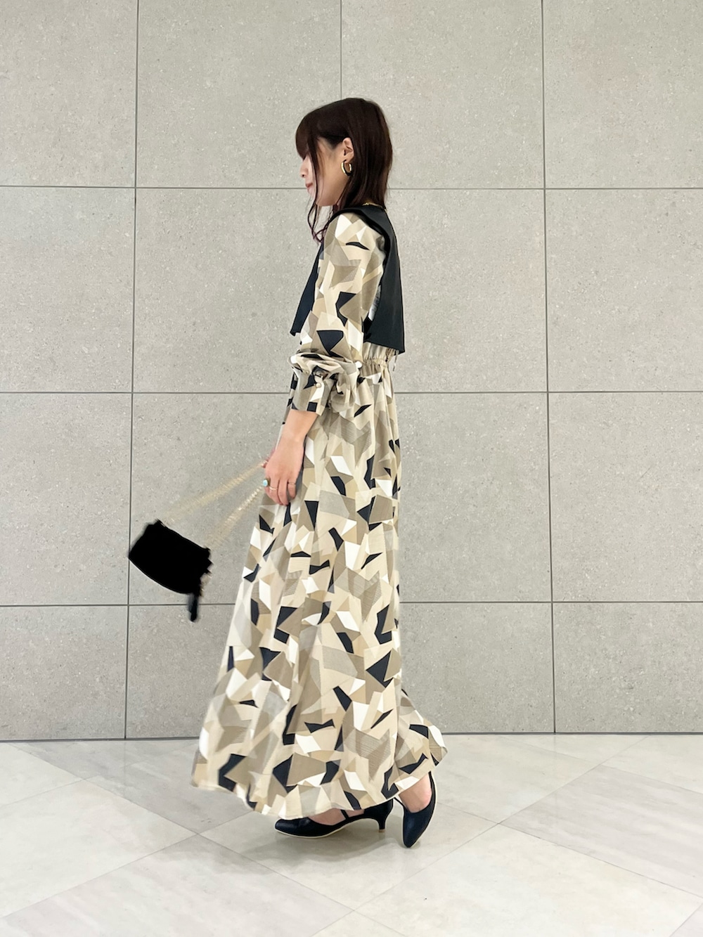 ベージュ系のワンピース、ブラック系のベスト、ブラック系のハンドバッグを着用したレディースの秋コーディネートの2枚目の写真