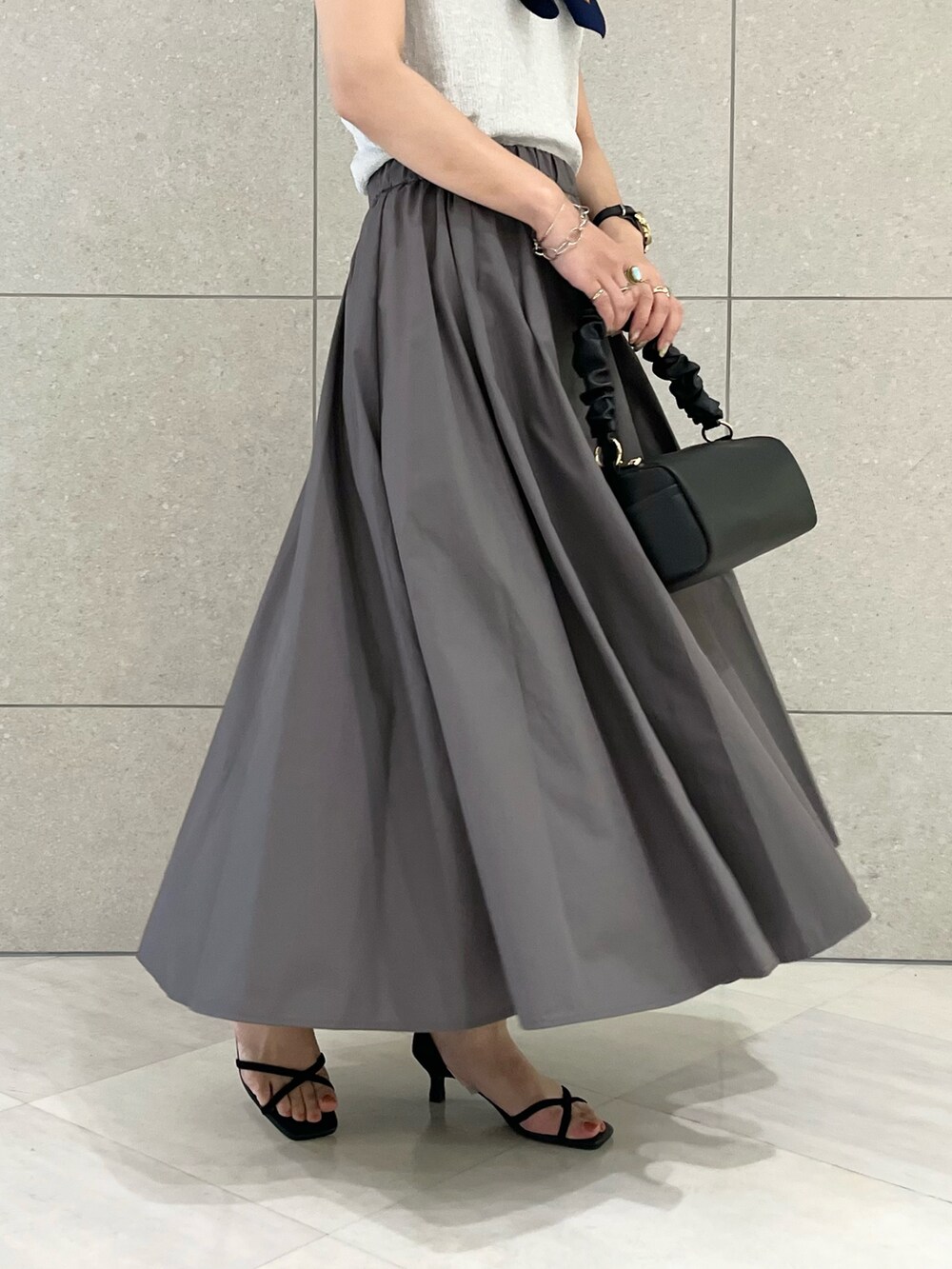 シルバー系のニット/セーター、グレー系のスカート、ブラック系のハンドバッグを着用したレディースの夏コーディネートの5枚目の写真