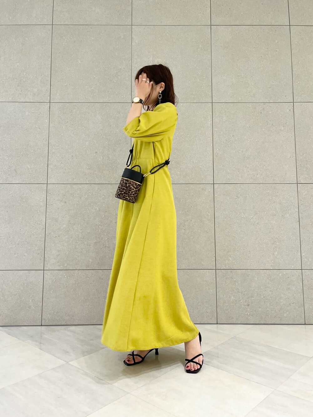 イエロー系のワンピース、ブラック系のハンドバッグ、ブラック系のサンダルを着用したレディースの春コーディネートの2枚目の写真