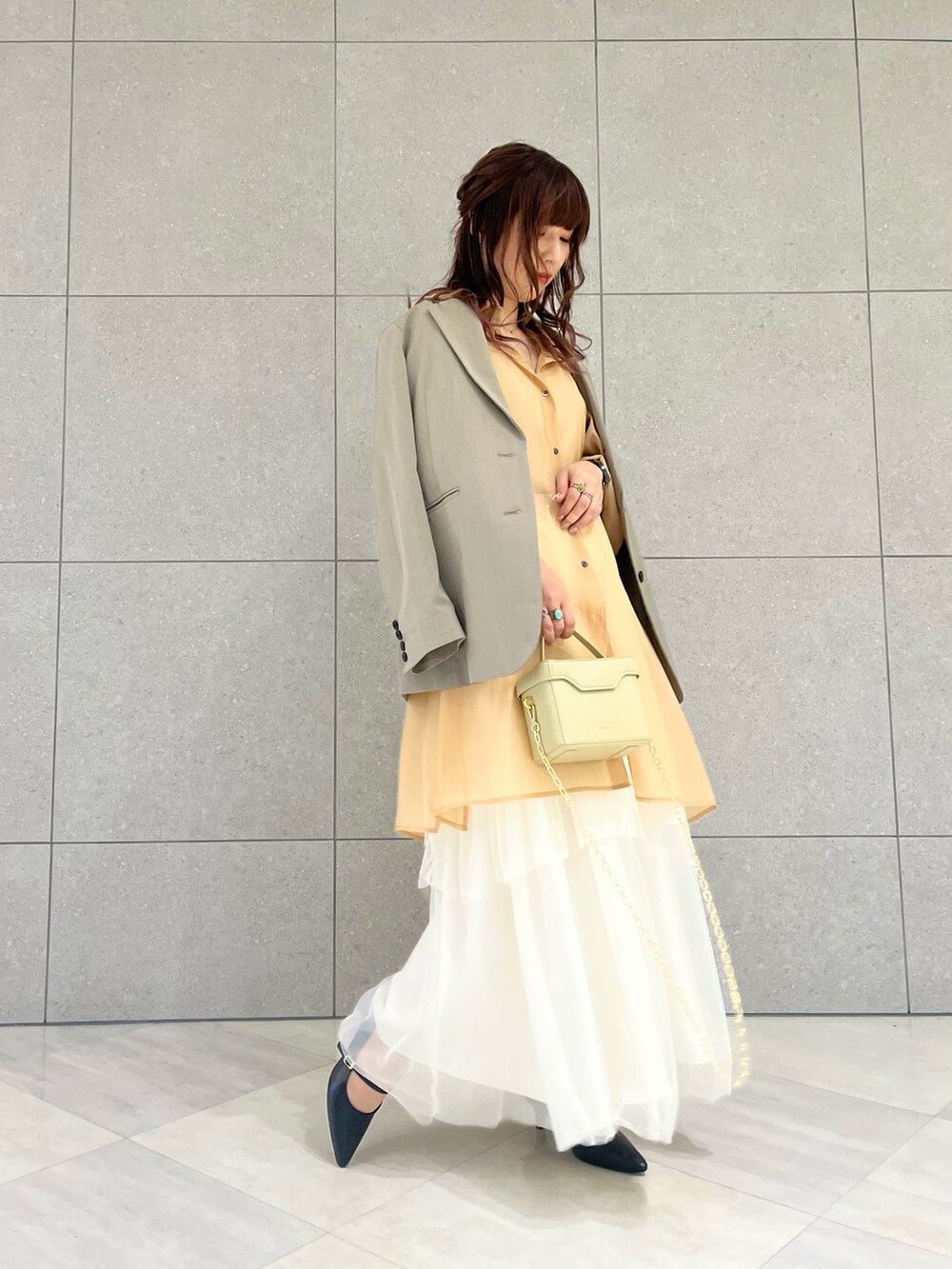 グリーン系のノーカラージャケット、ホワイト系のスカート、オレンジ系のワンピースを着用したレディースの冬コーディネートの2枚目の写真