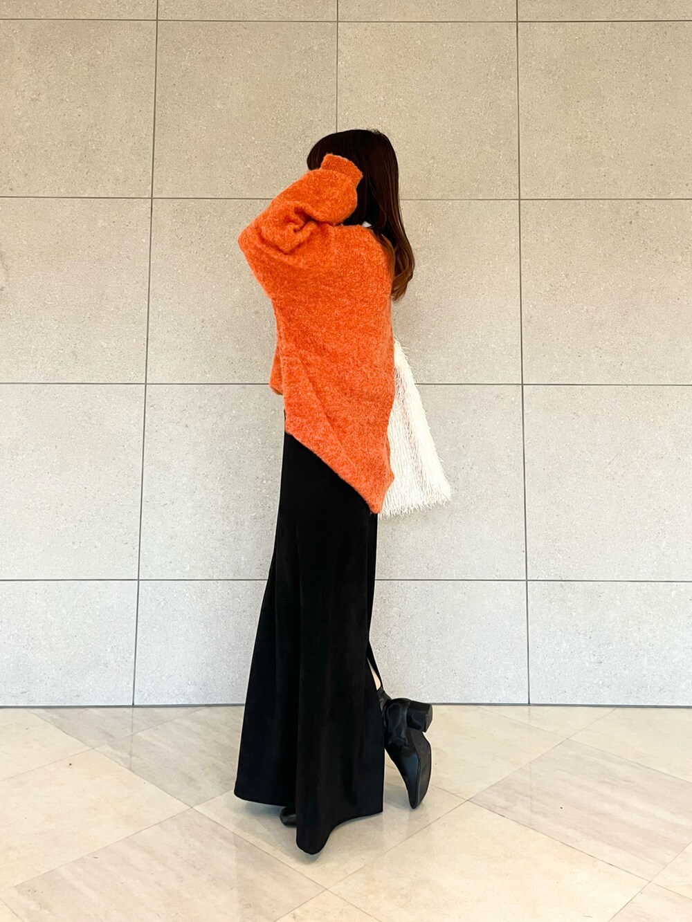 オレンジ系のニット/セーター、ホワイト系のハンドバッグ、ホワイト系のTシャツ/カットソーを着用したレディースの冬コーディネートの3枚目の写真