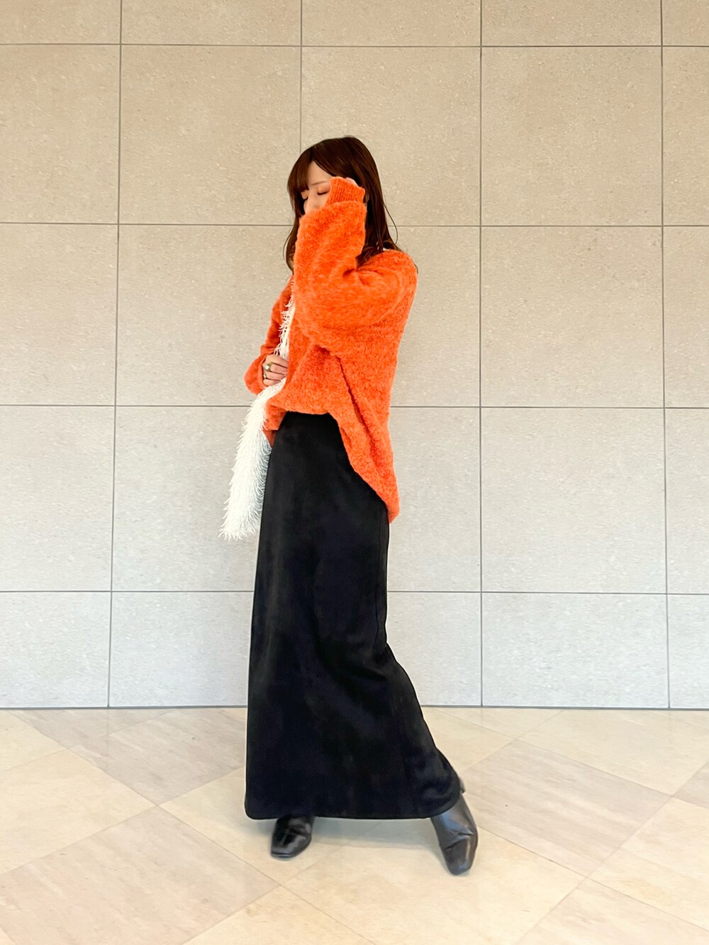 オレンジ系のニット/セーター、ホワイト系のハンドバッグ、ホワイト系のTシャツ/カットソーを着用したレディースの冬コーディネートの2枚目の写真