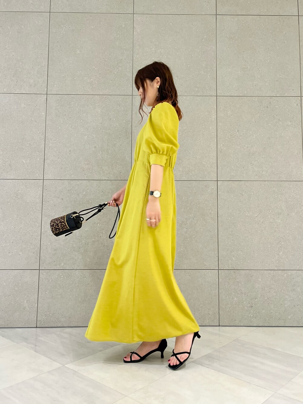 イエロー系のワンピース、ブラック系のハンドバッグ、ブラック系のサンダルを着用したレディースの春コーディネートの3枚目の写真