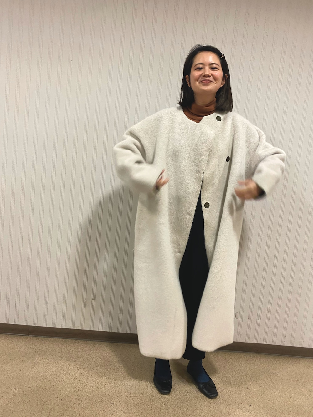 ベージュ系のその他アウター、オレンジ系のニット/セーター、ブラック系のその他パンツを着用したレディースの冬コーディネートの2枚目の写真