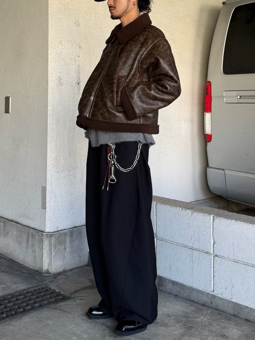 ブラック系のスラックス、グレー系のニット/セーター、ブラウン系のブルゾンを着用したメンズの秋コーディネートの4枚目の写真