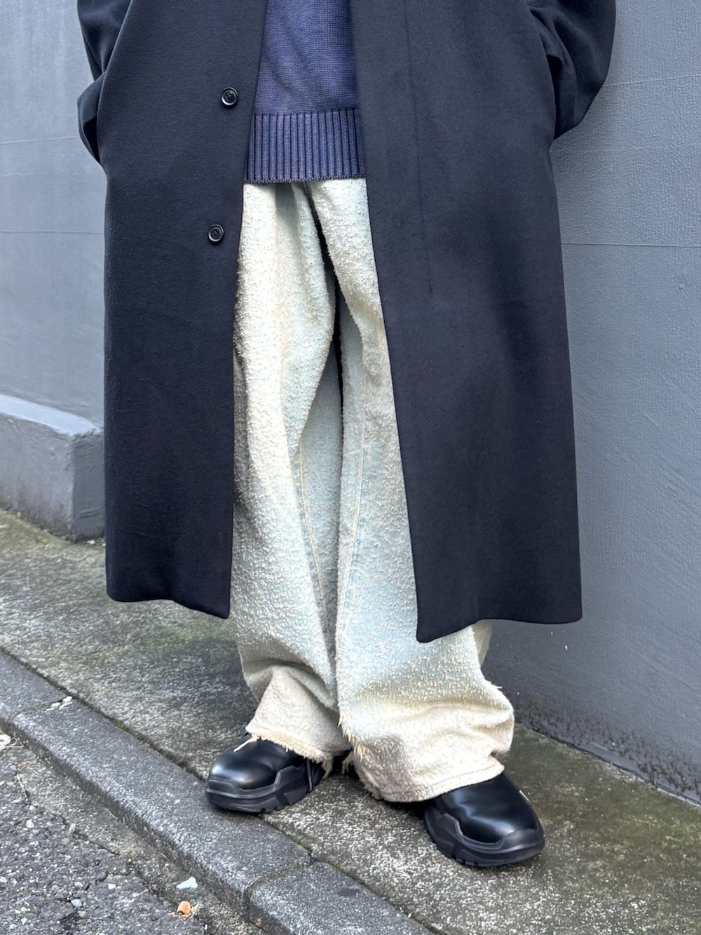 ブルー系のニット/セーター、ブルー系のデニムパンツ、ブラック系のステンカラーコートを着用したメンズの秋コーディネートの10枚目の写真